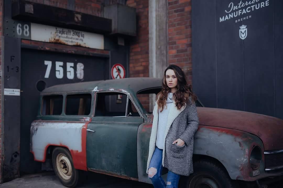 woman with brown hair white sweater gray jacket in front of old rusty vintage car featured photos