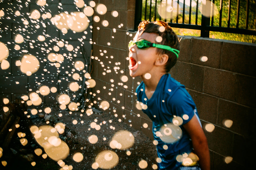 young boy in sprinkler happy wearing swim goggles